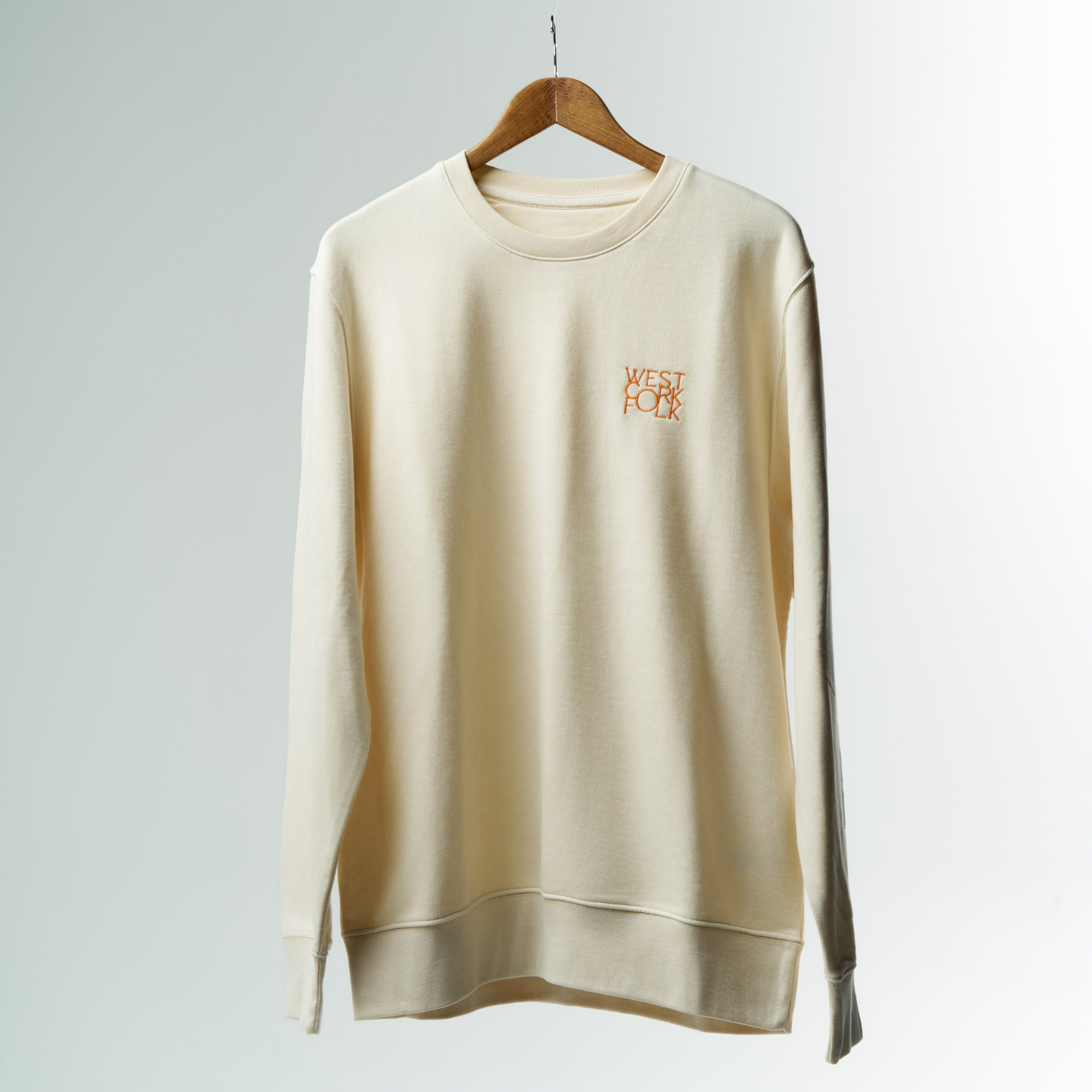 Beige sweatshirt with 'West Cork Folk' logo on a hanger against a grey background
