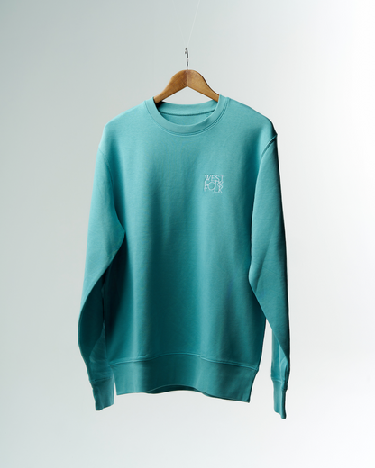 A turquoise West Cork Folk sweater with the logo embroidered on the chest, hanging on a wooden hanger against a white background.